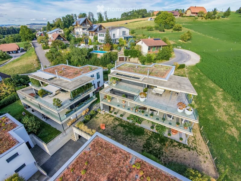 Aerial view of a modern residential complex with multiple buildings, green roofs, balconies, and surrounding greenery.