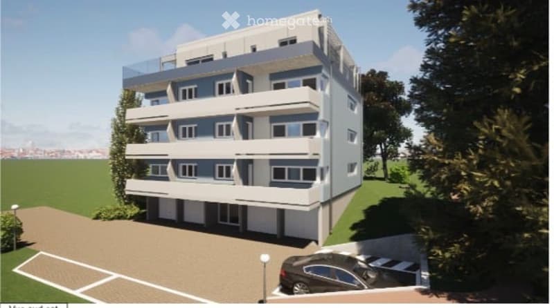 Modern multi-story apartment building with balconies, parking area, and landscaped surroundings.