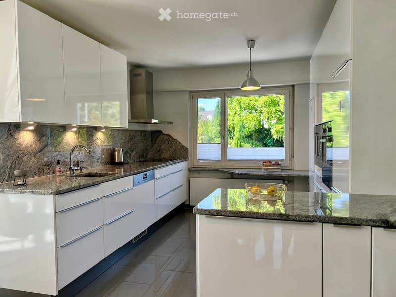Modern kitchen with white cabinets, granite countertops, stainless steel appliances, and a central island with a fruit basket.