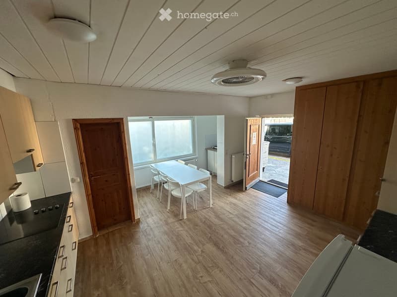 Open-plan kitchen and dining area with wooden flooring, white dining table and chairs, cabinets, and a sink.