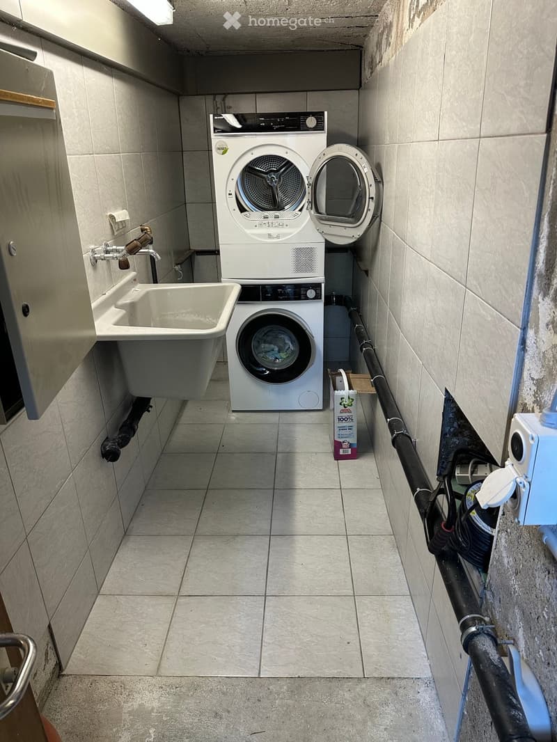 Compact bathroom with a washing machine, dryer, and sink, featuring tiled walls and floor.