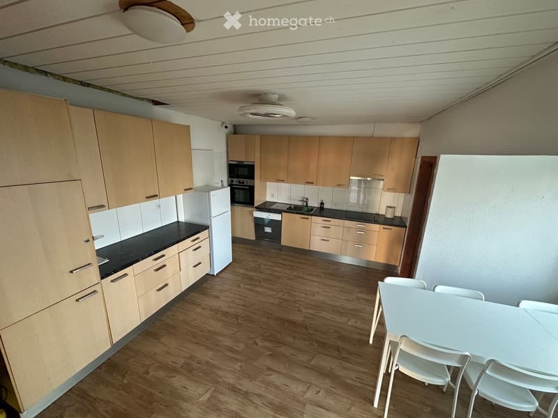 Modern kitchen with light wood cabinets, black countertops, stainless steel appliances, and a small dining area with a white table and chairs.