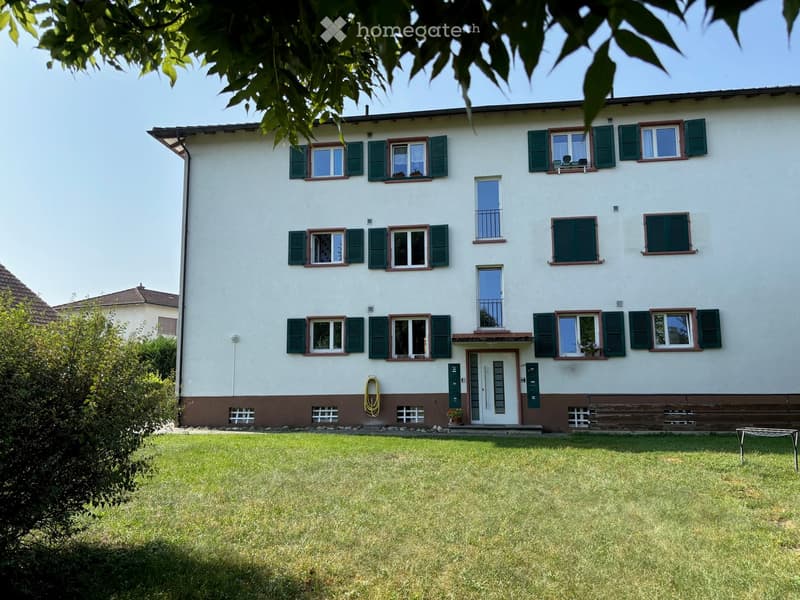 Multi-unit apartment building with white exterior, green shutters, and a garden in the front.