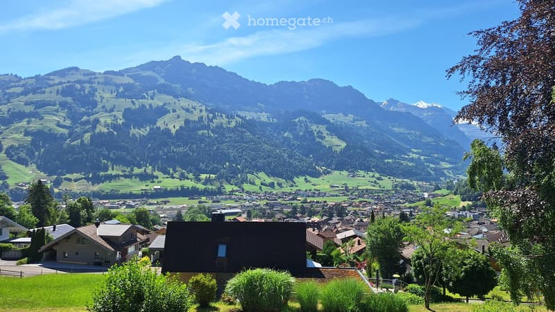 A scenic view of a town nestled in a valley surrounded by lush green hills and mountains, with a clear blue sky overhead.