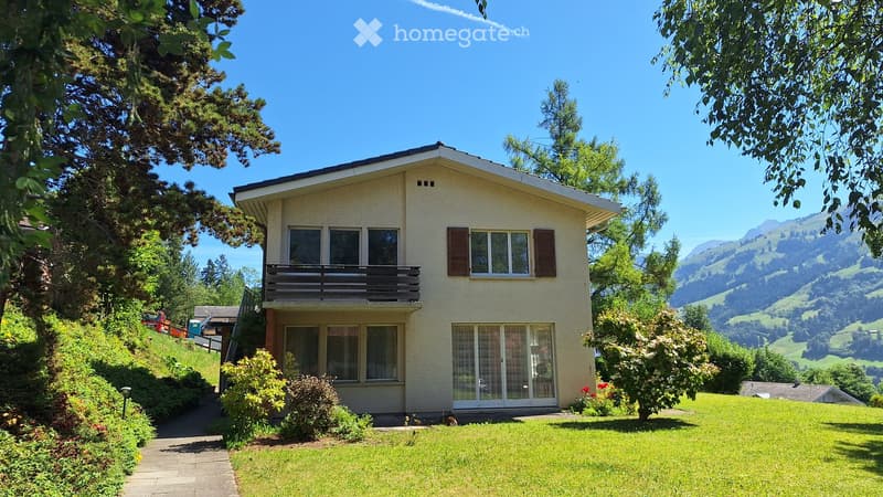Two-story house with a balcony, surrounded by greenery and a scenic mountain view.