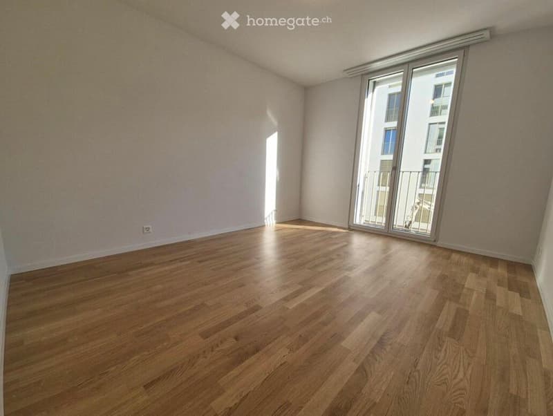 Empty room with wooden flooring and large sliding glass doors leading to a balcony. Light-colored walls and natural light from the windows.