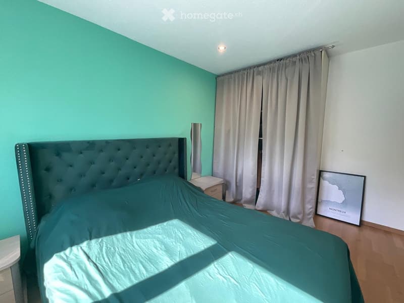 Bedroom with teal walls, a dark green upholstered bed, a nightstand, a mirror, and a framed picture on the wall.