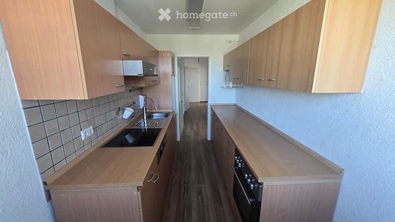 Modern kitchen with wooden cabinets, a sink, and an oven. The floor is wooden, and the walls are tiled in the kitchen area.