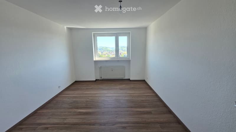 Empty room with wooden flooring, white walls, and a window offering a view of the landscape.