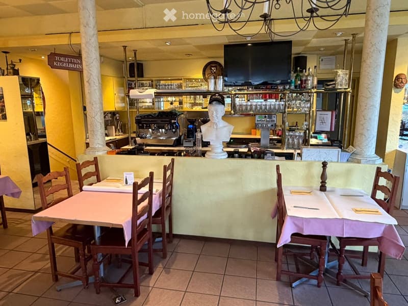 A restaurant interior with tables and chairs, a television, a refrigerator, a coffee machine, and a statue in the center.