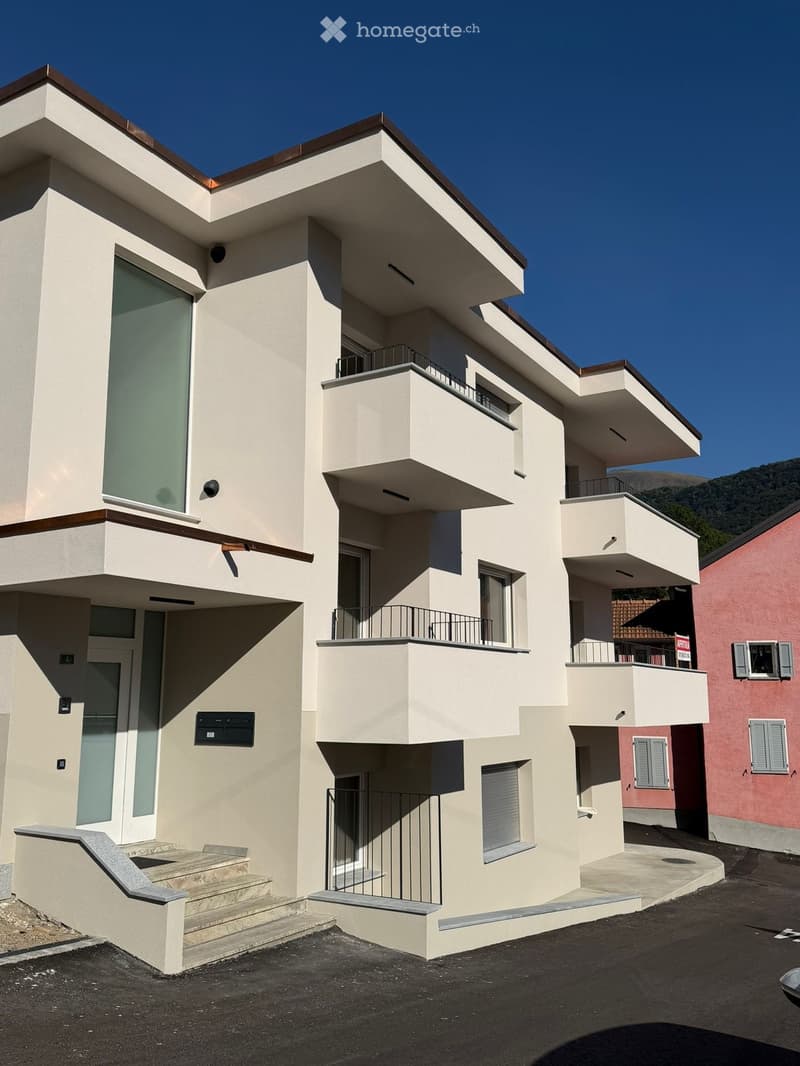 Modern two-story house with beige facade, large windows, balconies, and a staircase leading to the entrance.