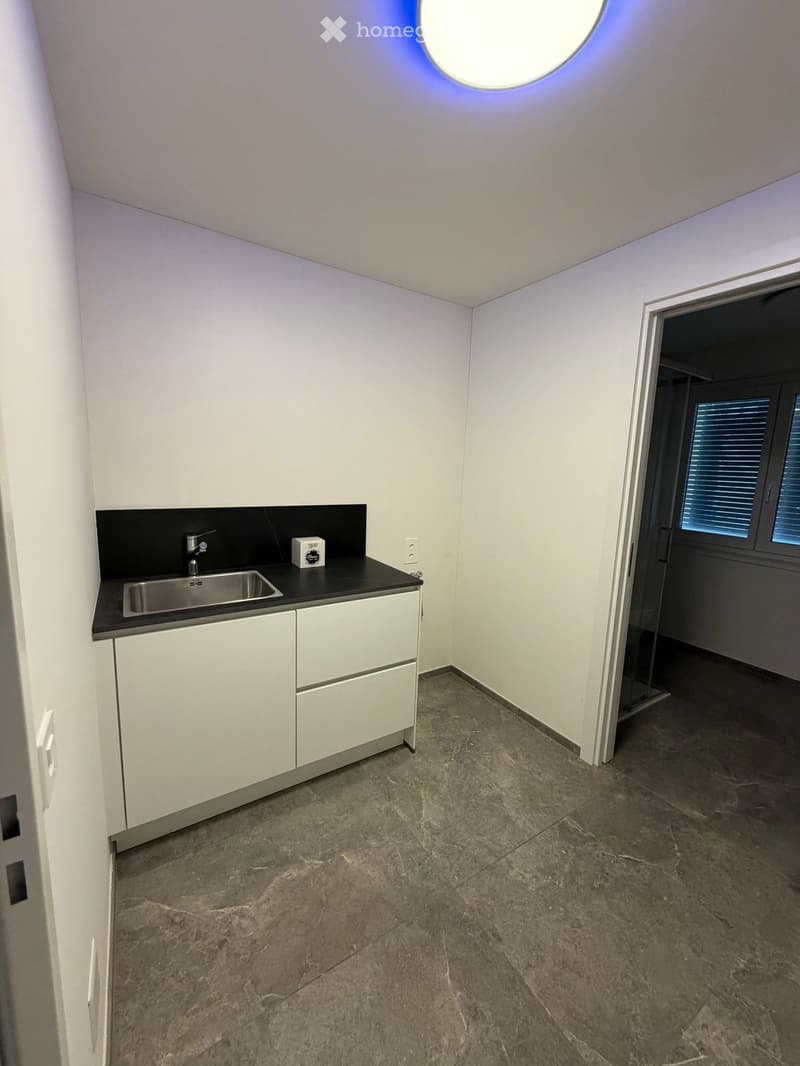 Empty kitchen with white cabinets, a stainless steel sink, and a dark countertop. The floor is made of polished stone tiles, and there is a circular skylight above.