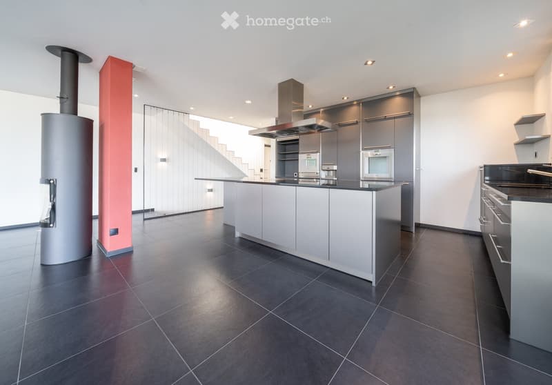 Modern kitchen with grey cabinets, a central island, stainless steel appliances, and a dark tiled floor.