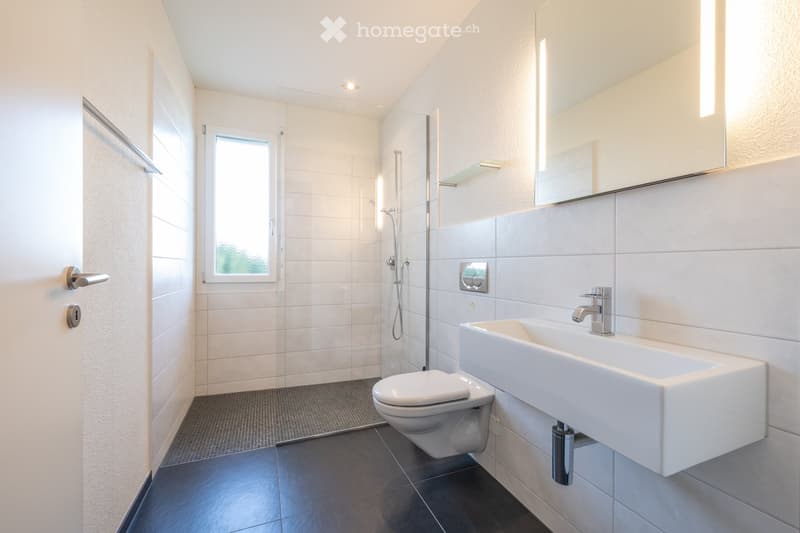 Modern bathroom with white tiles, a large mirror, a sink, a toilet, and a glass-enclosed shower area.