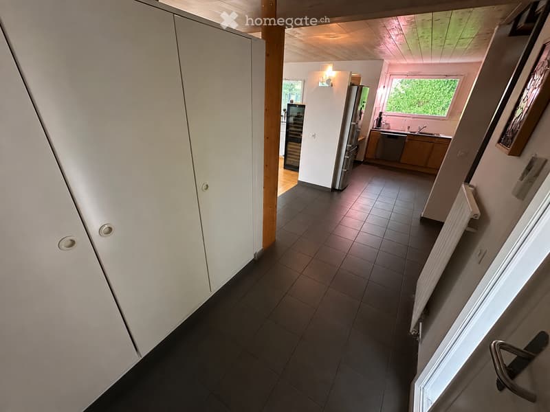 A modern hallway with dark tiled flooring, white walls, and a wooden door frame leading to a kitchen area with stainless steel appliances and wooden cabinets.