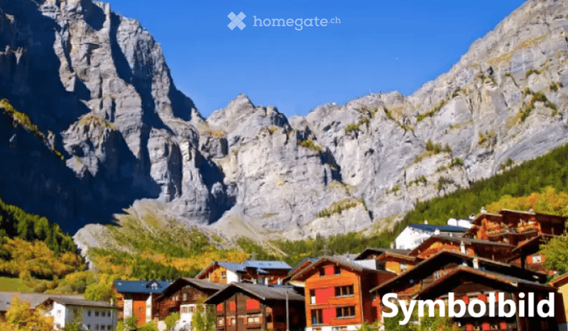 Village with traditional wooden houses nestled in a valley surrounded by towering mountains under a clear blue sky.