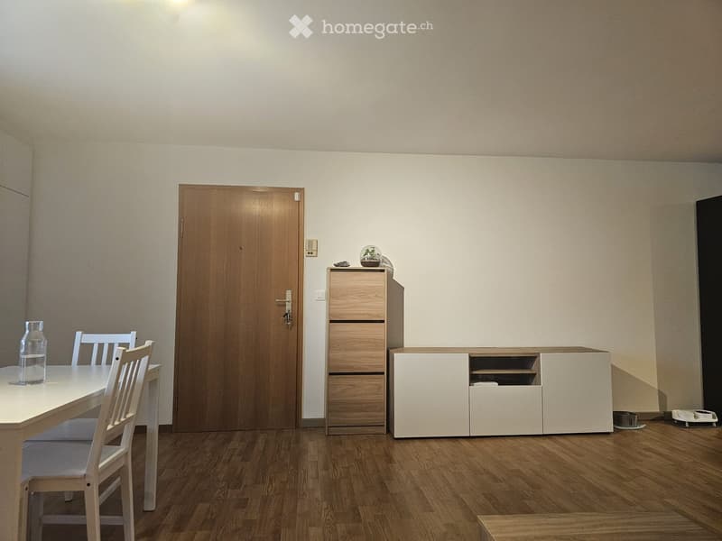 Dining room with a wooden dining table, chairs, a cabinet, and a white cupboard. The room has light-colored walls and wooden flooring.