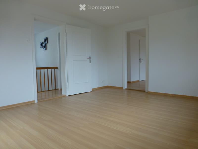 Empty room with light wooden flooring, white walls, and open doorways leading to other rooms. No furniture or equipment is present.