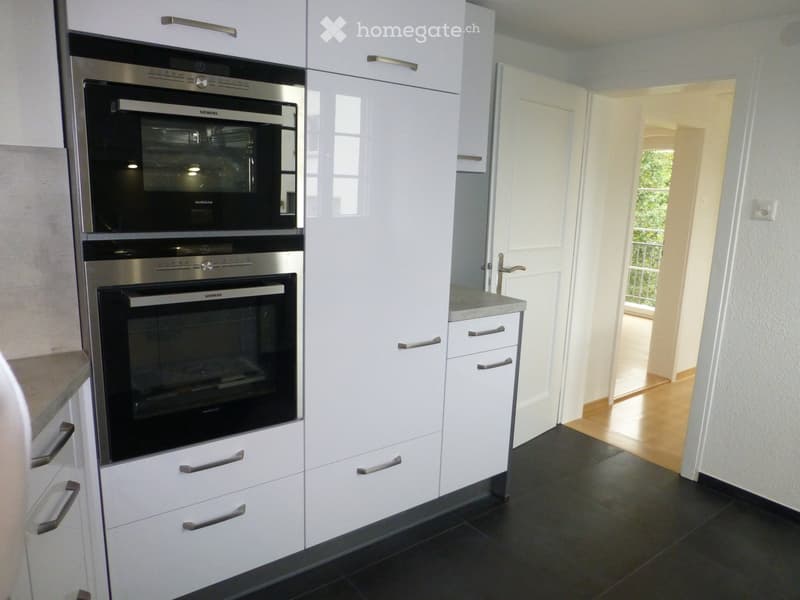 Modern kitchen with white cabinets, stainless steel oven, and black tiled floor.
