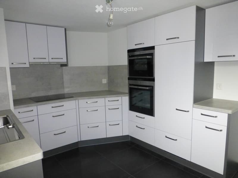 Modern kitchen with white cabinets, stainless steel oven, and black tiled floor.