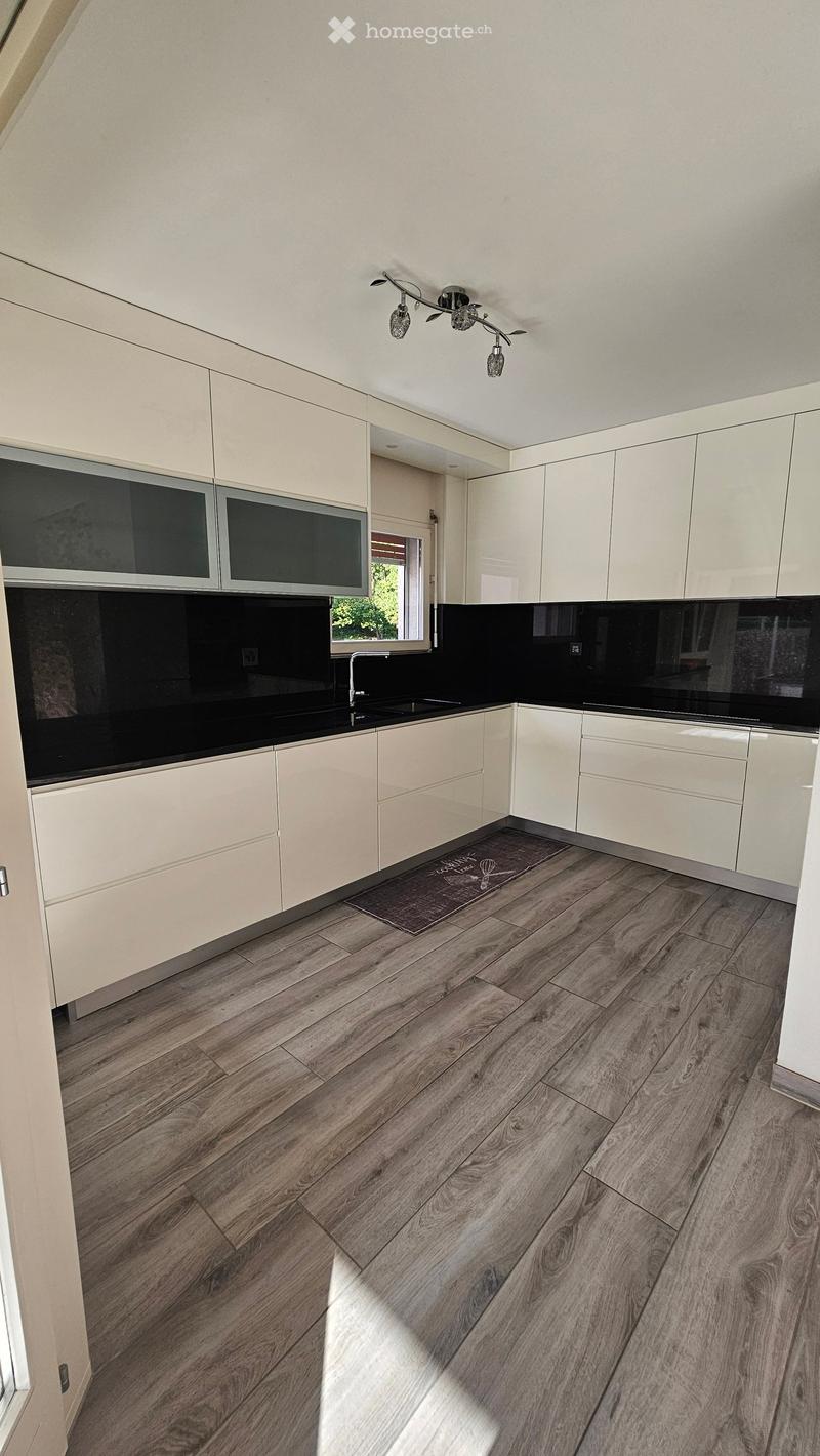 Modern kitchen with light-colored cabinets, dark countertops, and wooden flooring.