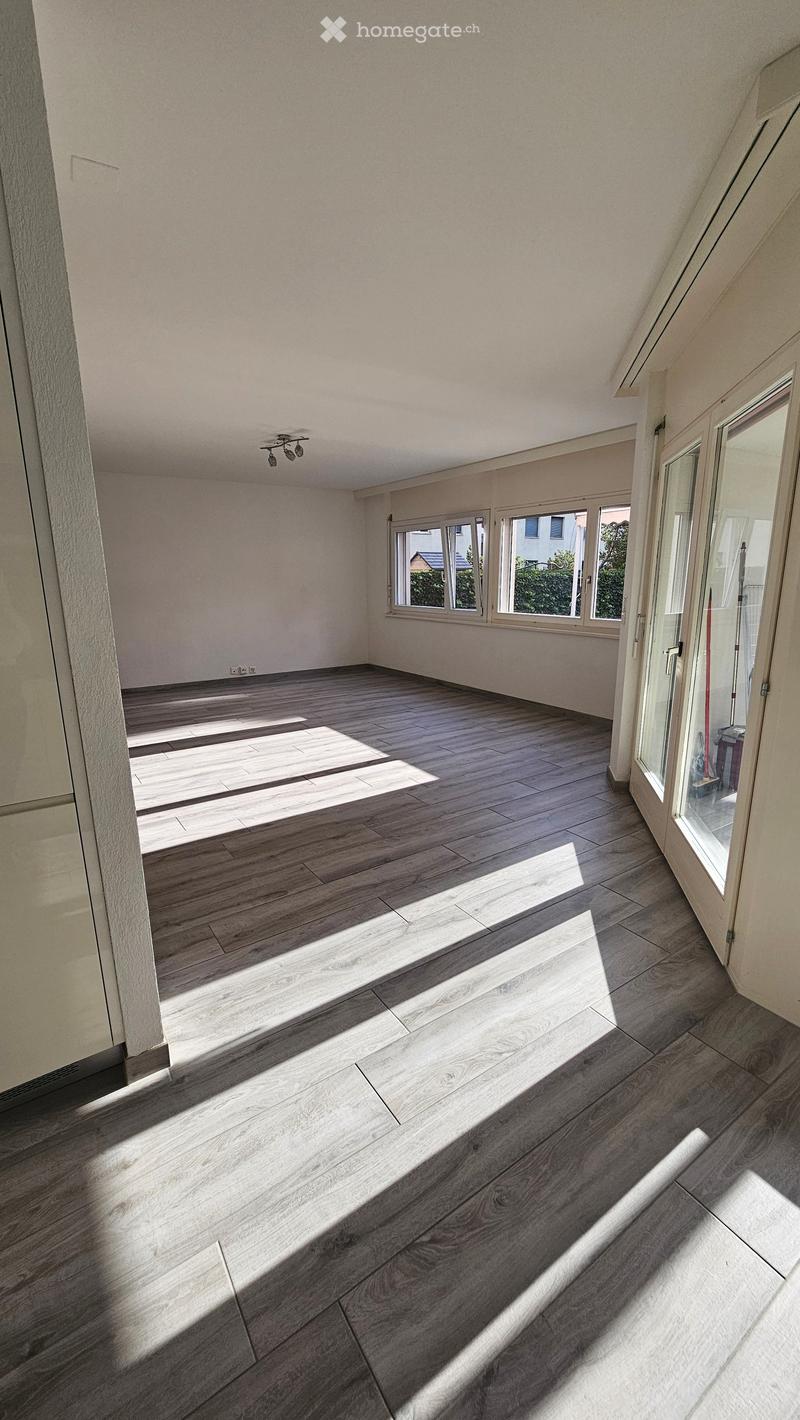 Empty room with wooden flooring and large windows allowing natural light to enter. The space is unfurnished and appears to be a living or dining area.