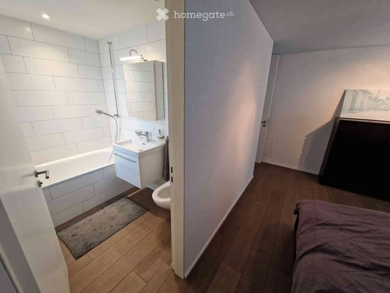 Bathroom with white tiled walls, a white bathtub, white sink, and toilet. White ceiling and walls, wooden floor.