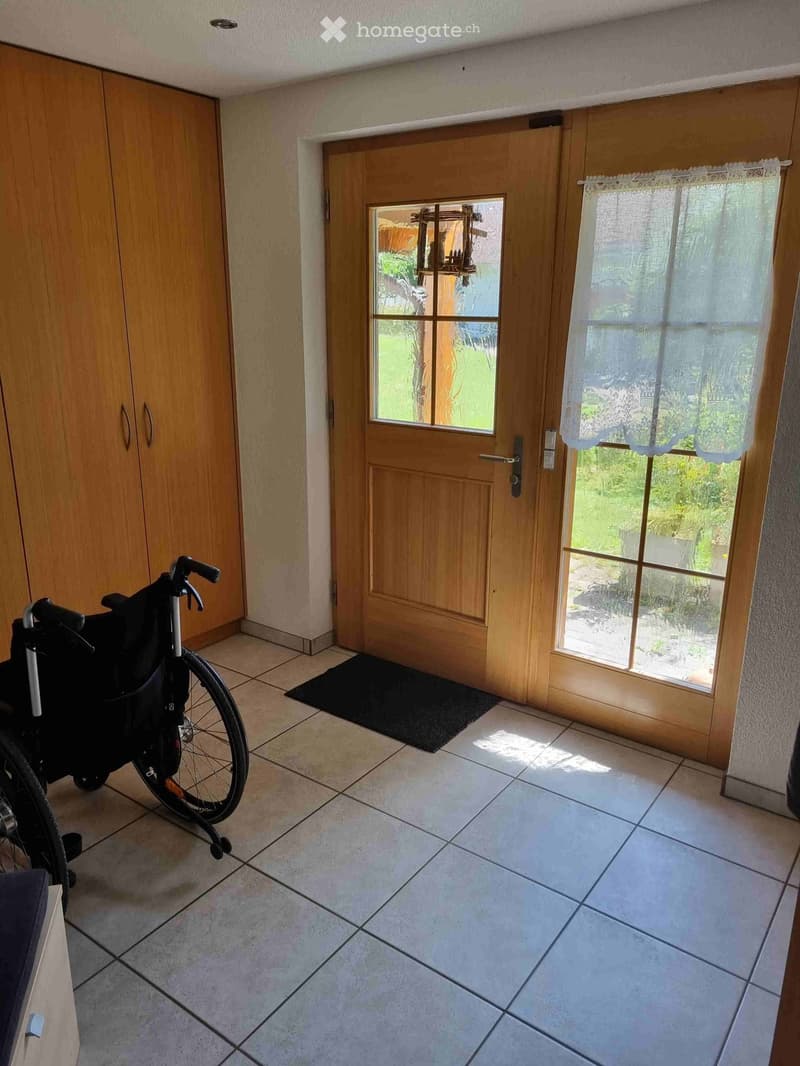 Hallway with tiled floor, wooden door leading outside, and a wheelchair parked near the door.