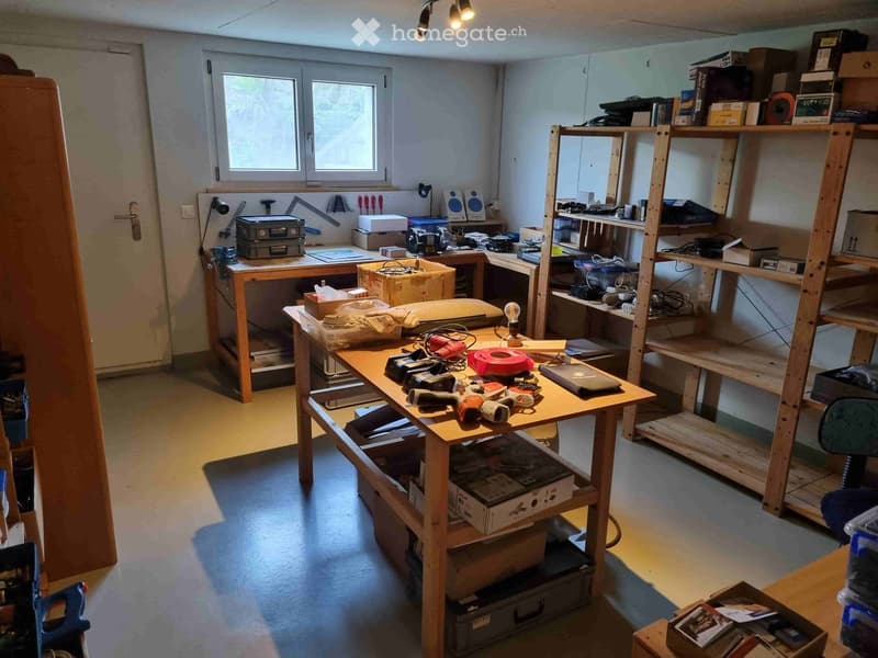 Workshop or storage room with wooden tables, shelves, tools, and boxes.