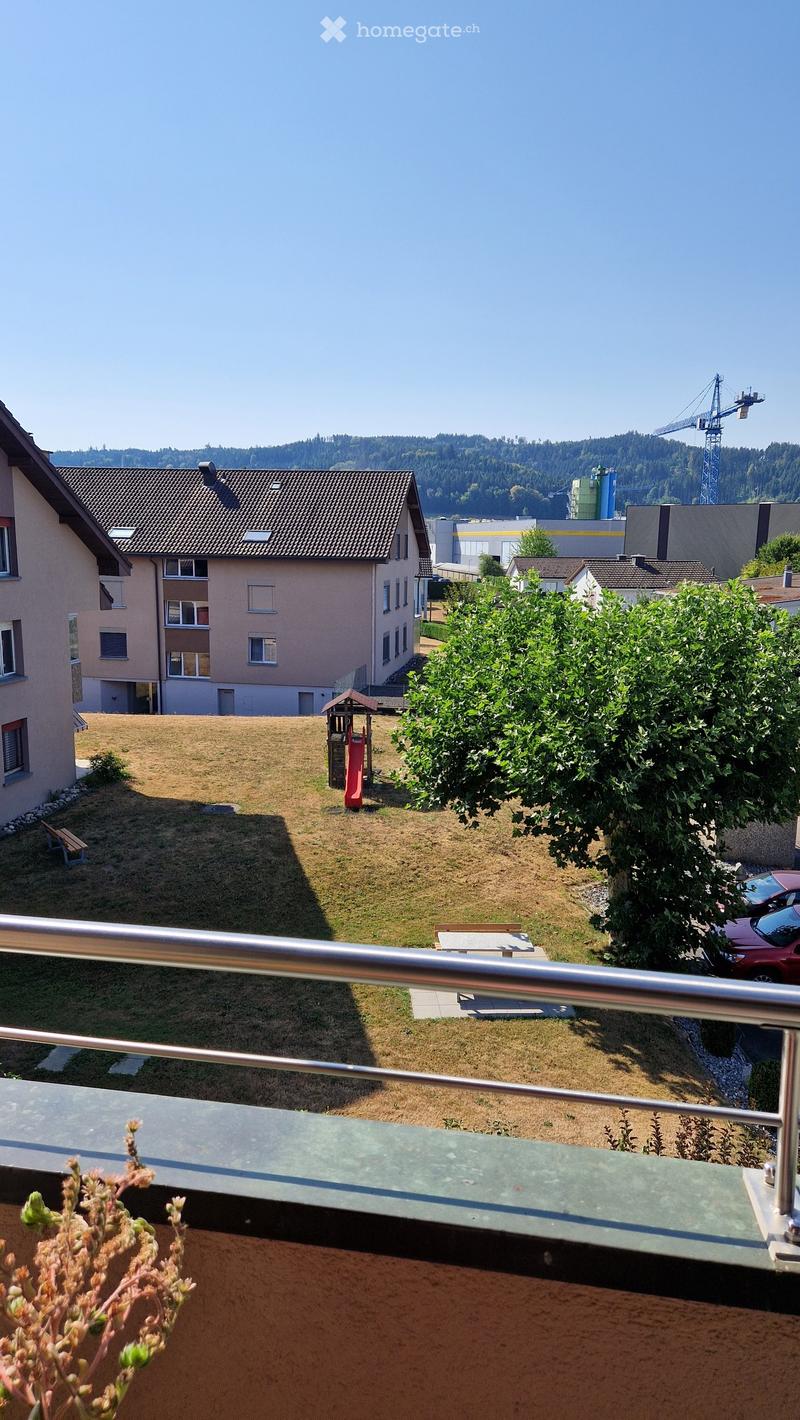 View from a balcony overlooking a grassy yard with a small play structure, benches, and surrounding residential buildings.