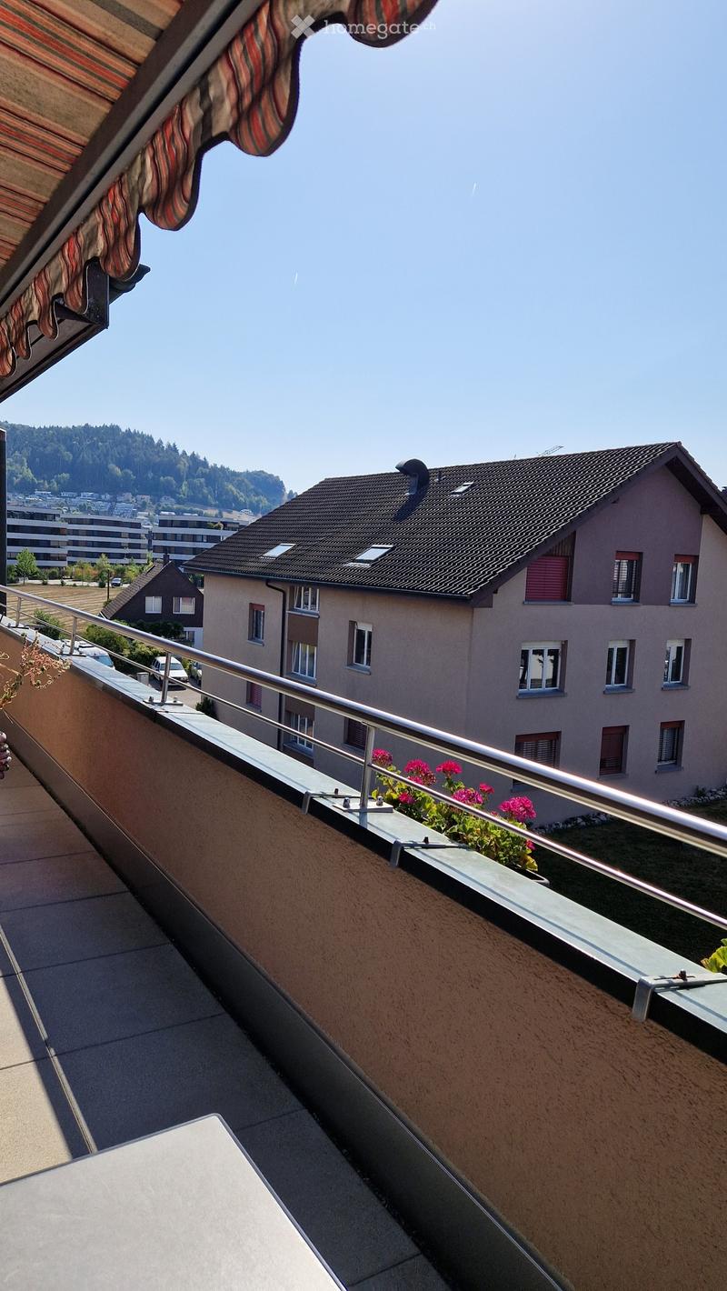 Balcony with metal railing, potted plants, and a view of neighboring houses and greenery.