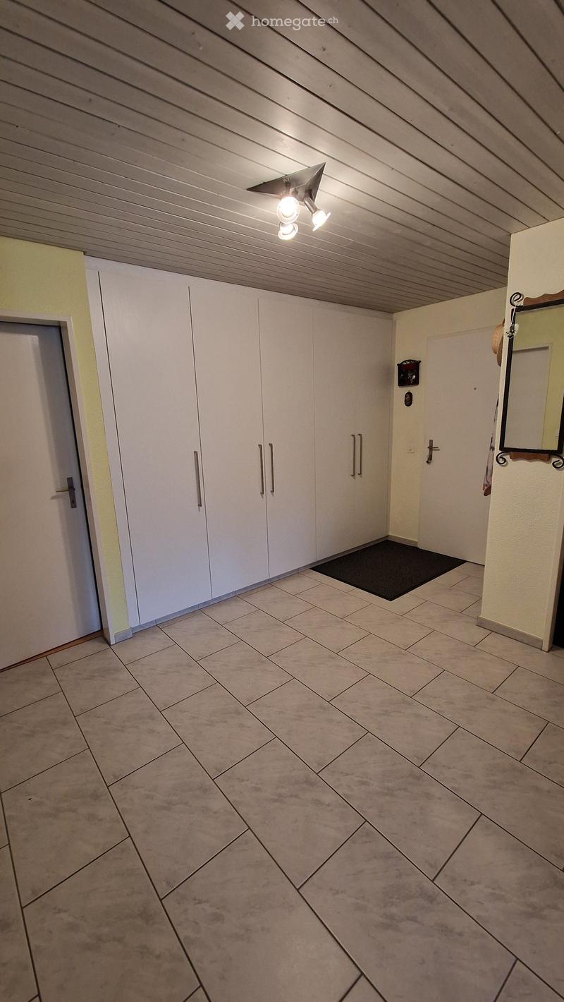 Empty hallway with tiled floor, white closet doors, and a small black doormat near the entrance.