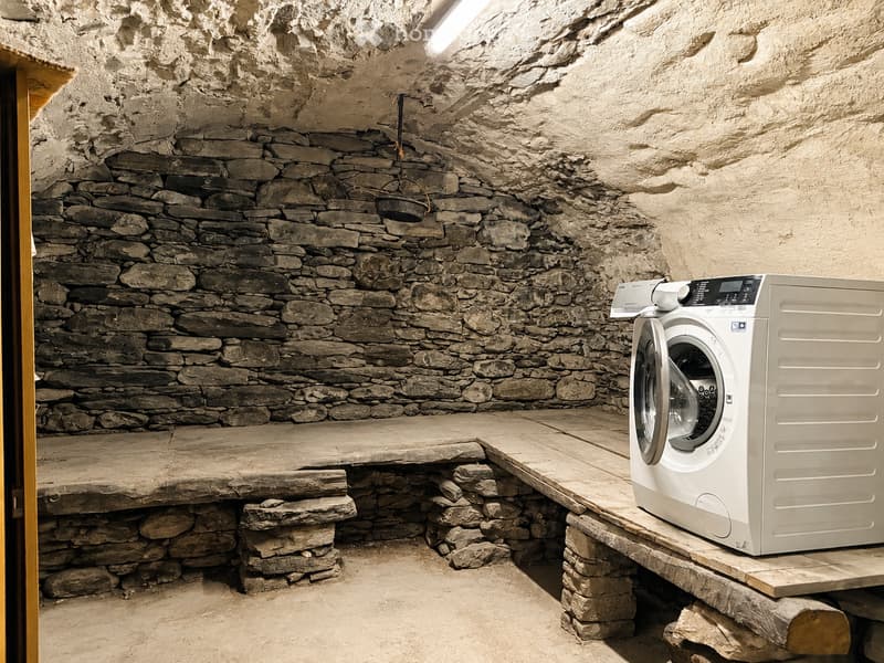 A rustic bathroom with stone walls and a wooden platform holding a modern washing machine.