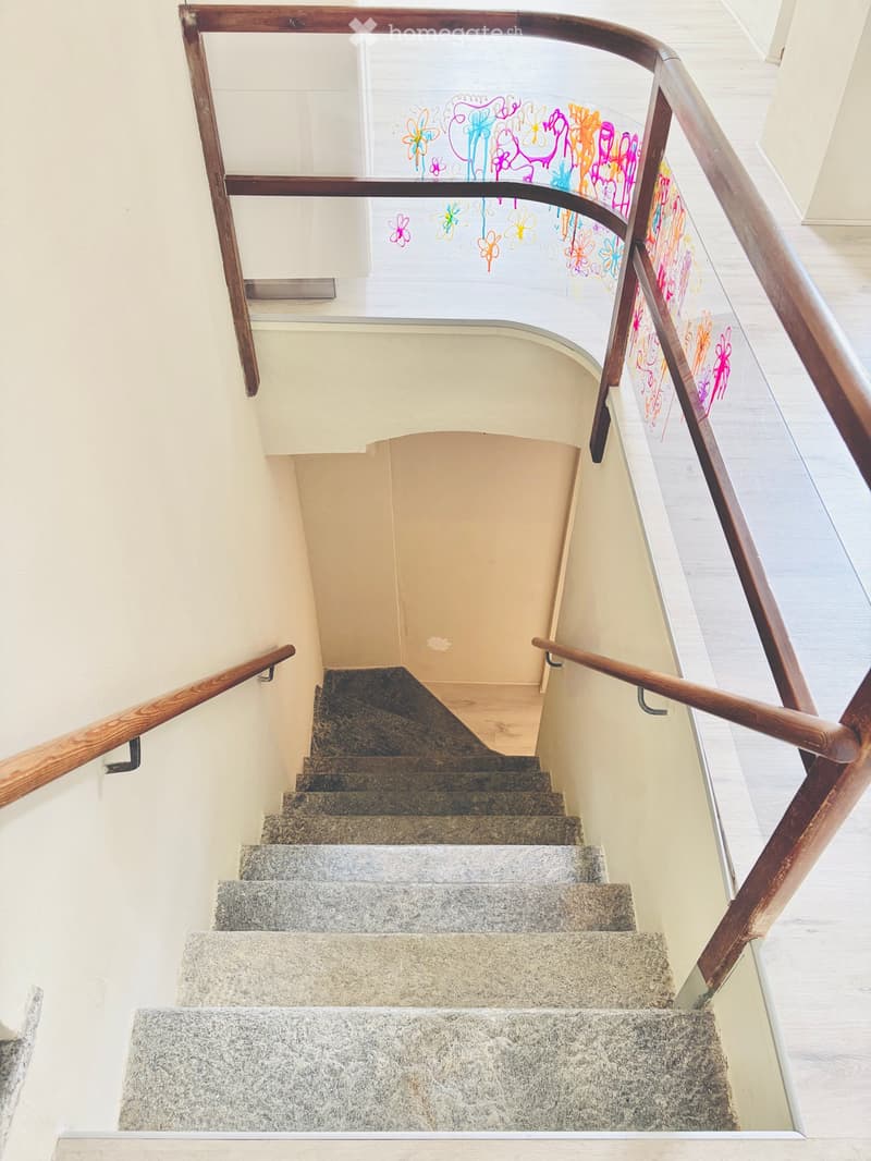 Spiral staircase with wooden handrails and granite steps, featuring colorful abstract artwork on the glass railing.