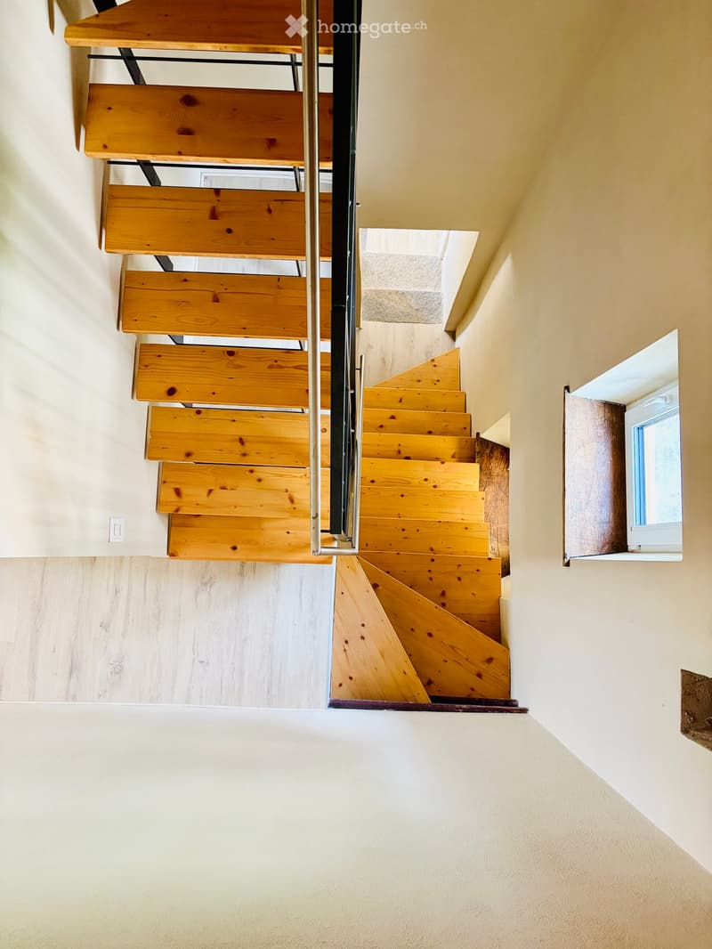 Wooden staircase with metal railing, light-colored walls, and a small window on the right side.