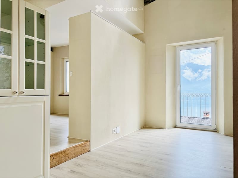 Empty room with light-colored walls, wooden flooring, and a sliding glass door leading to a balcony with a scenic view.