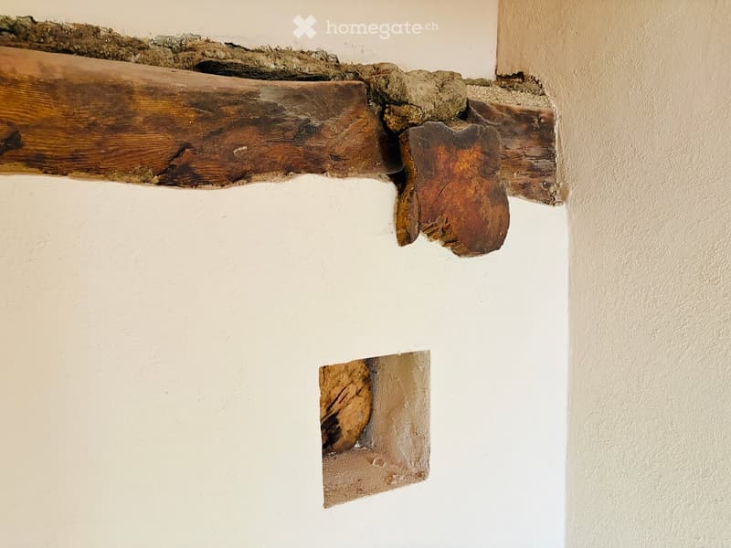 Close-up of a wall showing exposed wooden beams and patches of plaster, indicating a partially unfinished or renovated interior space.