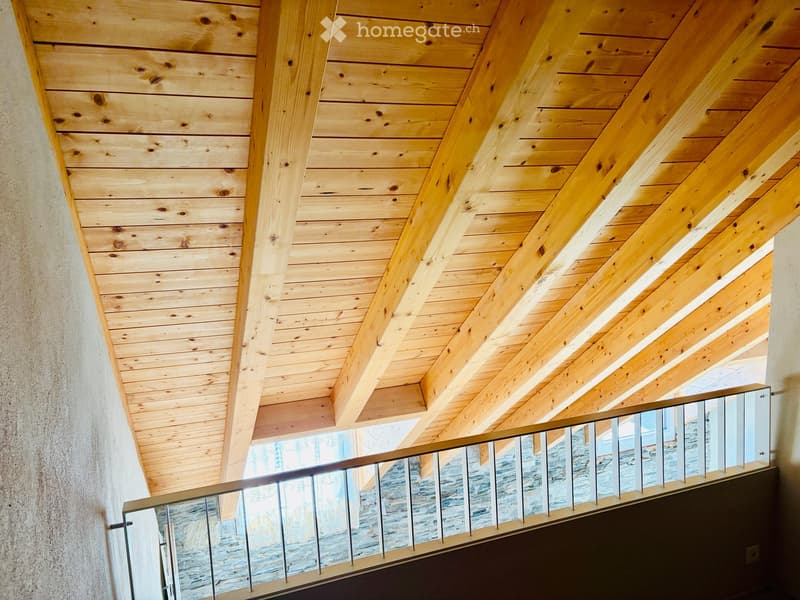 A modern hallway with exposed wooden beams and a sleek metal railing leading to a view of the outdoors.