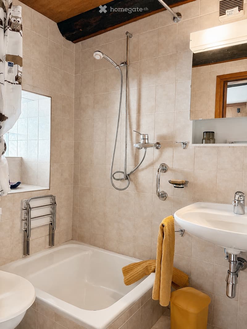 Bathroom with beige tiled walls, a bathtub, a sink, a showerhead, a mirror, and a towel hanging on a rack.