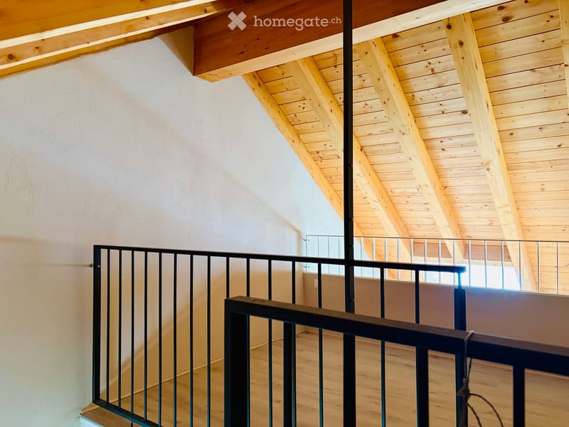 Staircase with wooden ceiling beams, metal railing, and light-colored wooden flooring.