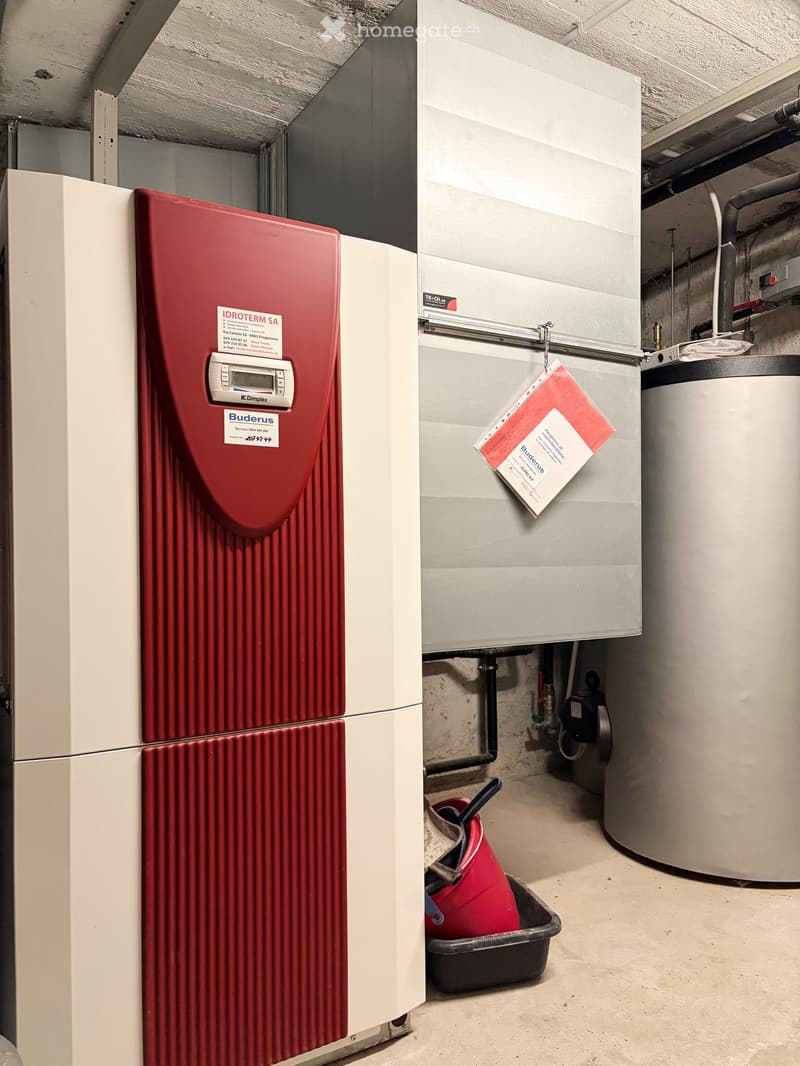 Utility room with a red water heater, grey boiler, and a red bucket on the floor.