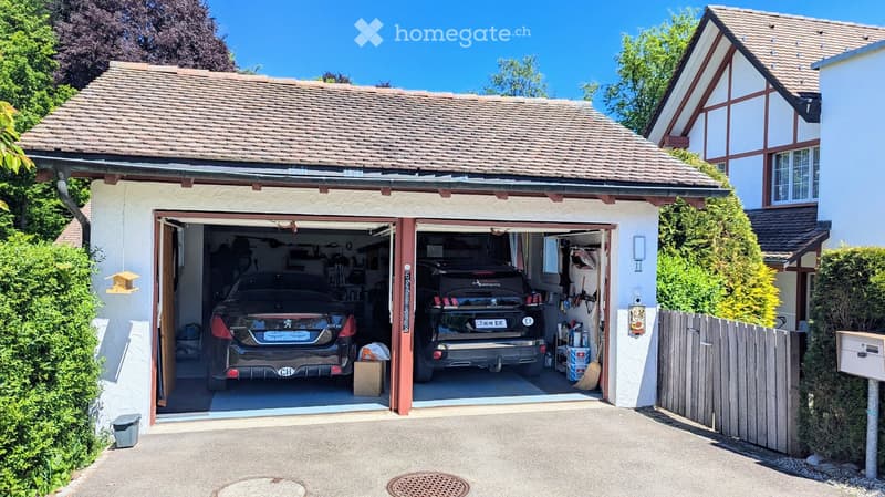 Two-car garage with two luxury cars inside, attached to a two-story house with a tiled roof and white exterior.