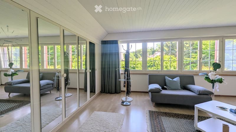Modern living room with large windows, grey sofa, white coffee table, coat rack, and decorative mirrors.