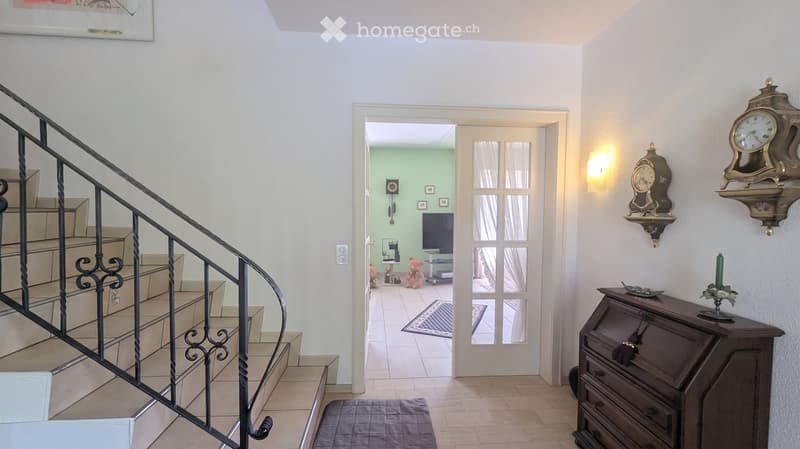 Hallway with a staircase, a doorway leading to a living room, and decorative wall clocks.