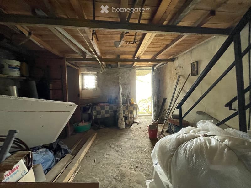 Unfurnished attic space with exposed wooden beams, concrete floor, and scattered items including tools, buckets, and a staircase leading upwards.