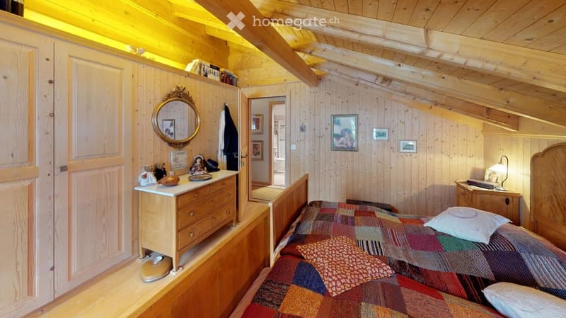 Cozy wooden bedroom with slanted ceilings, a single bed with a colorful quilt, a nightstand with a lamp, a dresser with a mirror, and decorative items on the walls.