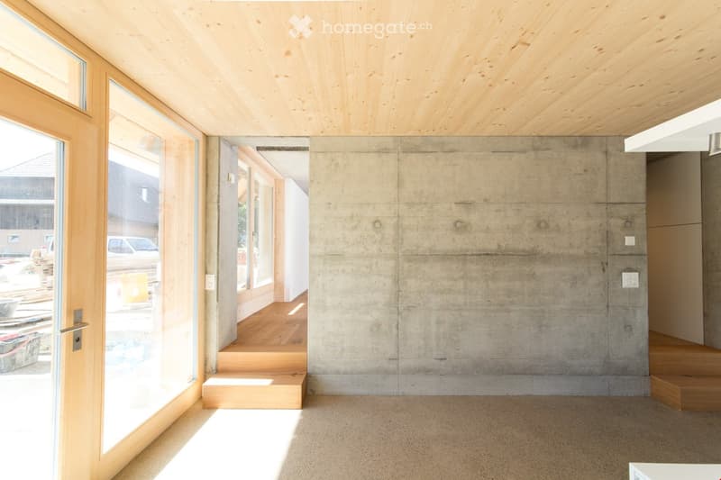 Modern hallway with exposed wooden ceiling, concrete walls, large glass doors leading to another room, and wooden steps.