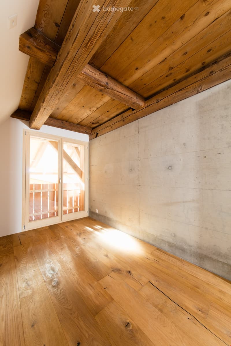 Empty room with wooden floor, exposed wooden beams on the ceiling, and a glass door leading outside.