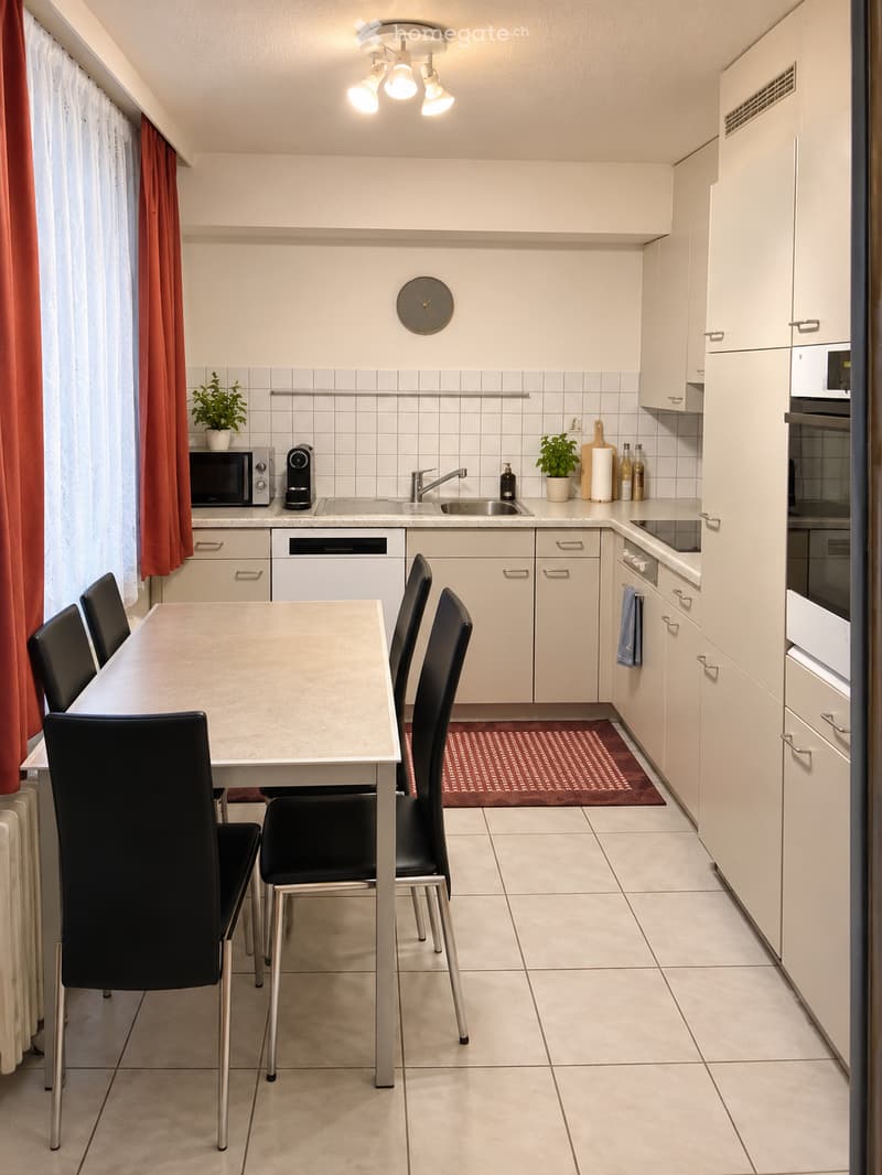 Modern kitchen with white cabinets, a dining table with four chairs, microwave, coffee maker, sink, and various appliances.