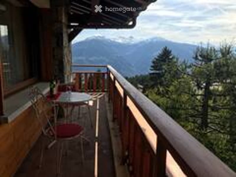 Balcony with wooden railing, outdoor furniture including a table and chairs, scenic mountain view in the background.
